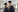 A picture of a couple in graduation robes and a hat facing each other smiling 